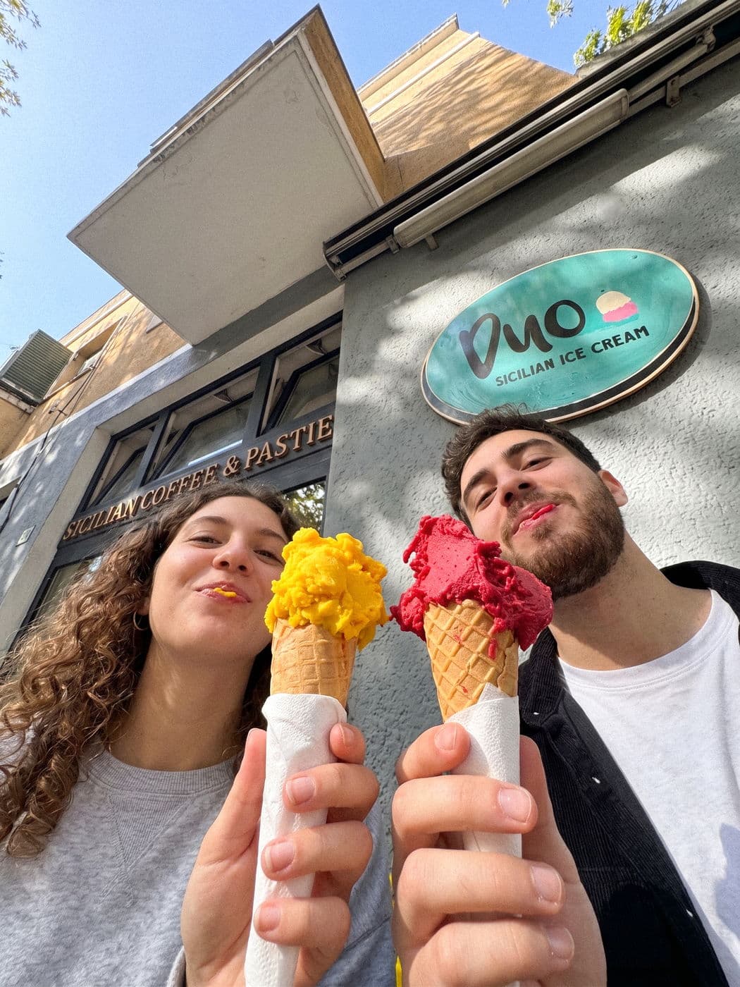 Two mango and raspberry gelato cones held up in front of a Duo shop front